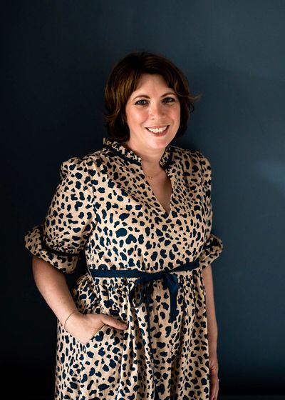 Jane Griffin wearing a leopard print dress and standing against a blue wall, smiling.