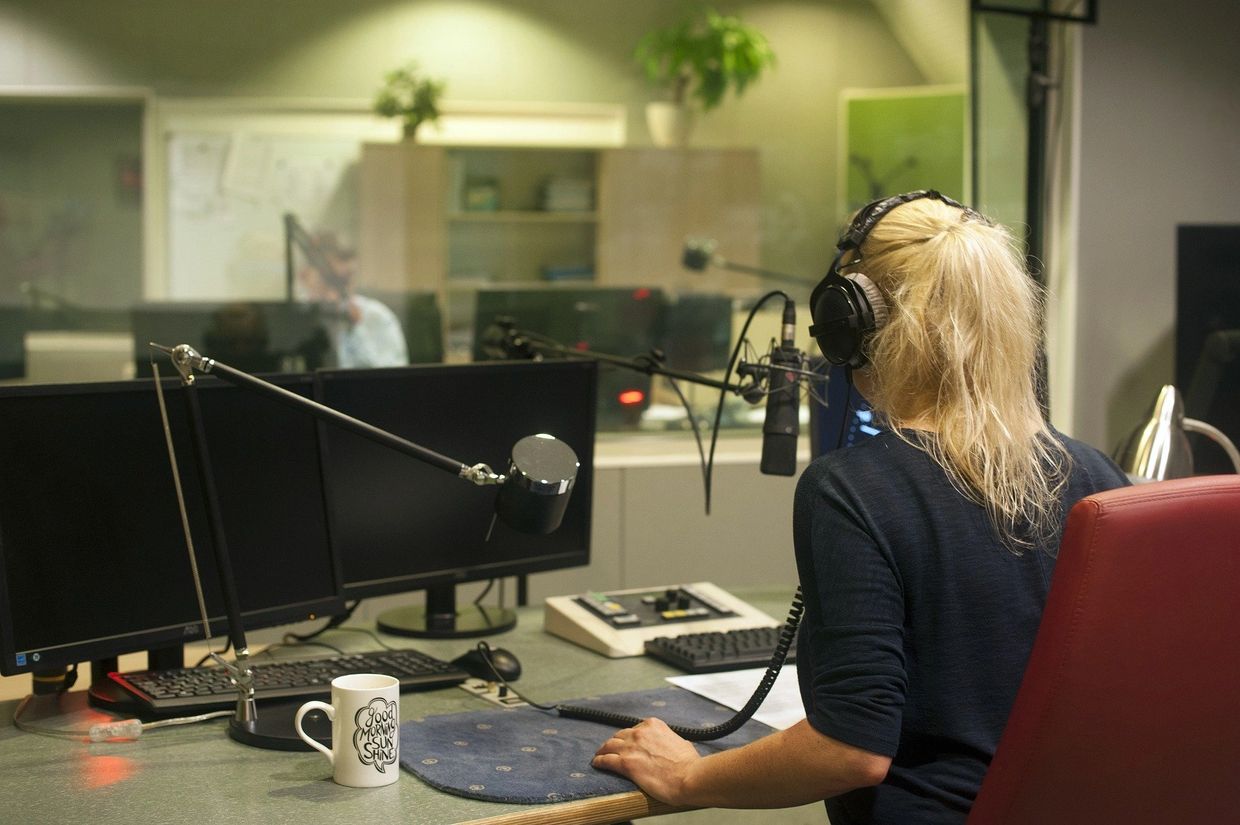 Woman with headphones on sitting in front of microphone in radio studio.