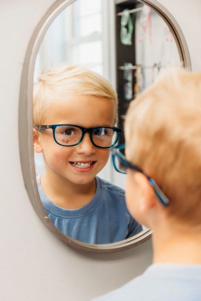 Boy wearing green glasses smiling at his reflection.