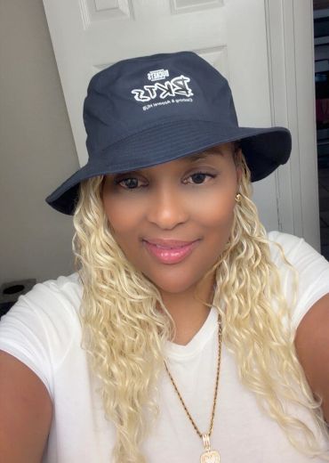 Woman with blonde hair wearing a black bucket hat and white shirt.