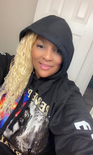 Smiling woman with blonde curly hair in a black hoodie.