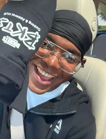 Happy young man smiling in car wearing glasses and black head wrap.