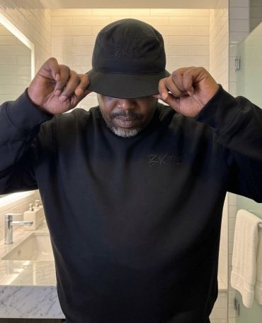 Man in black sweatshirt and hat adjusting his cap.