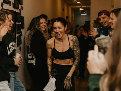 A woman with tattoos laughs surrounded by a happy crowd.