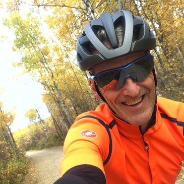Man in bright orange cycling gear takes a selfie on a forest trail in autumn.