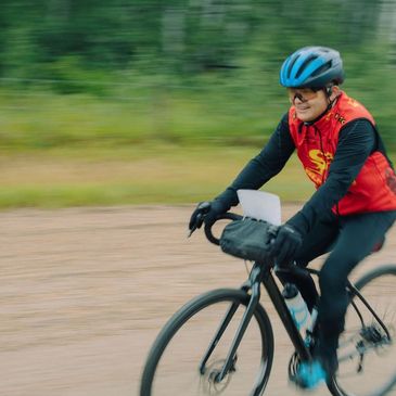 Cyclist in red jacket riding a black bike on a gravel path.