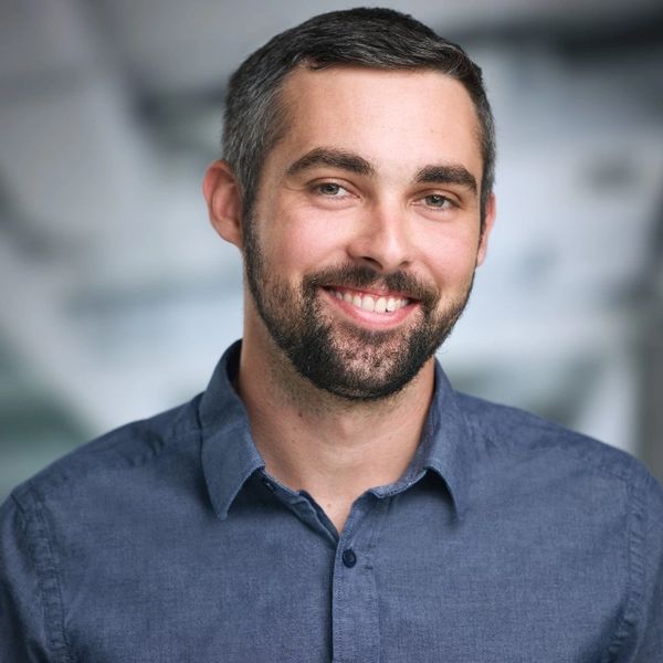Smiling man with beard in a buttoned shirt, black and white portrait.