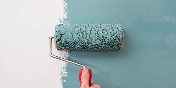 Hand painting wall with blue-green paint using a roller.