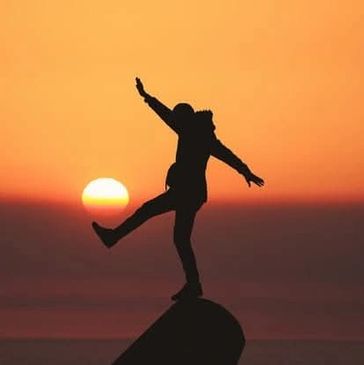 Silhouette of a person balancing on a rock at sunset.