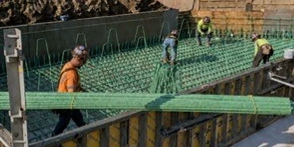 Workers handling green rebar at a construction site.