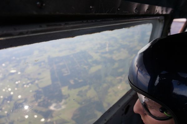 Person wearing helmet looking out airplane window.