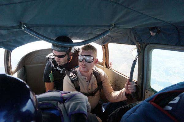 Two men inside an airplane wearing parachute gear.