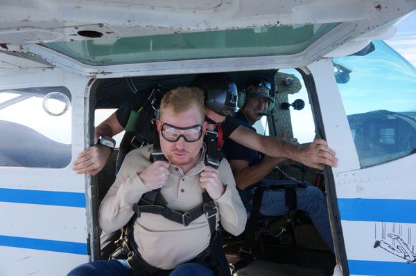 Three men preparing for a skydiving jump from a small plane.