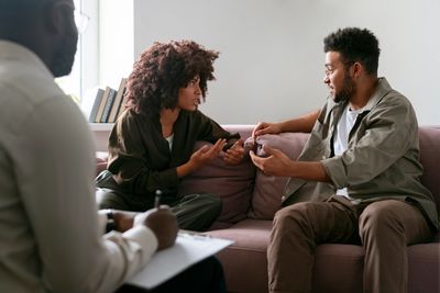 Couple discussing issues during therapy session with counselor taking notes.