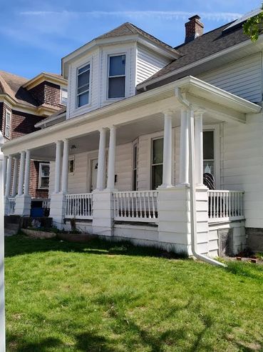 White house with a porch and a white picket fence under a clear blue sky.