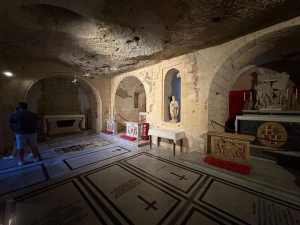 Dimly lit ancient crypt with stone arches and religious sculptures.