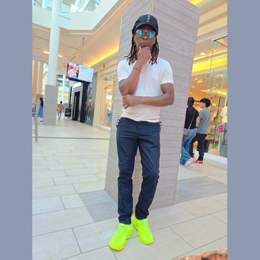Man in neon yellow shoes, white shirt, and blue jeans posing indoors.