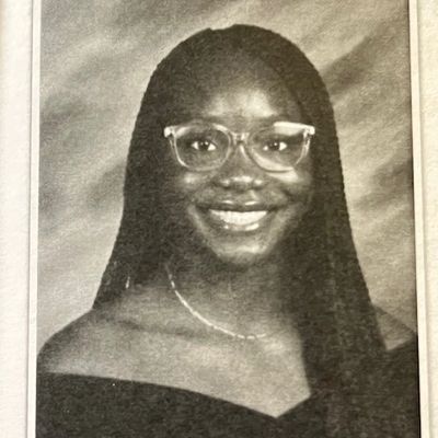 Smiling young woman with long hair and glasses in a formal portrait.