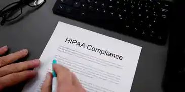 Person signing a HIPAA Compliance document at a desk with keyboard and glasses.