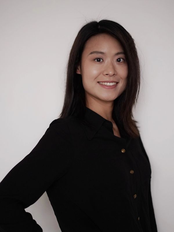 Smiling woman with dark hair wearing a black shirt against a plain background.