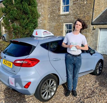 Young man proudly holding a practical driving test pass certificate by a learner car.