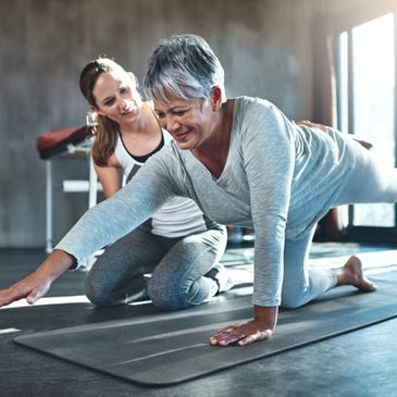 Senior woman doing yoga with instructor assistance indoors.