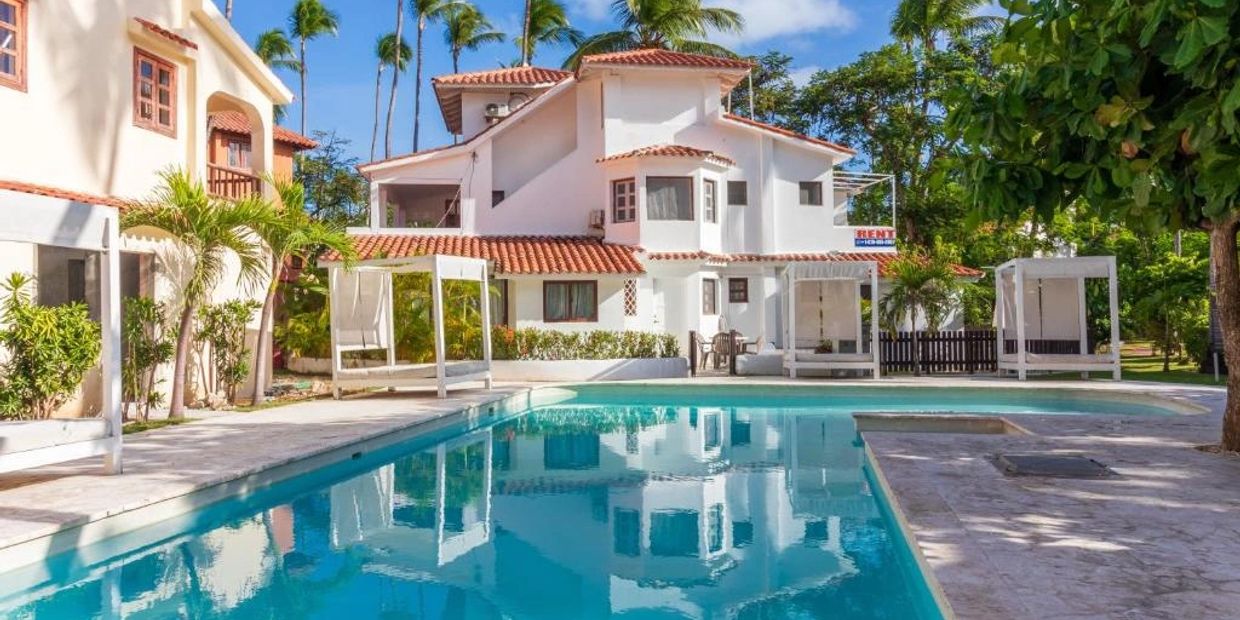 A white villa with a swimming pool and palm trees under a blue sky.
