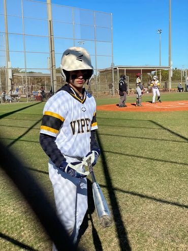 Young baseball player in white and yellow uniform prepares to bat on a sunny day.