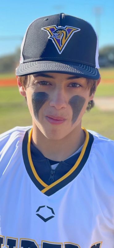 Young baseball player wearing a cap and eye black, standing on field.
