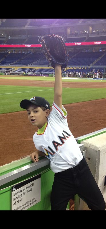 A young boy in Miami Marlins gear catching a baseball glove at a stadium.