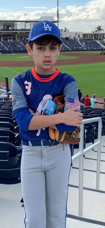 Young baseball player in uniform holding glove and phone at stadium.