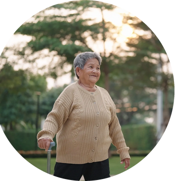 Elderly woman smiling outdoors with a walking cane, surrounded by greenery.