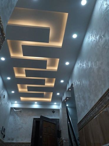 Modern ceiling design with recessed warm lighting and spotlights in a hallway.