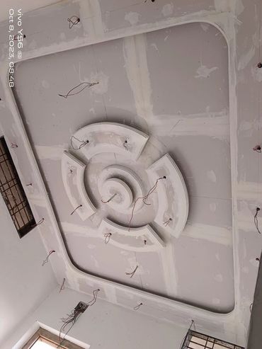 Ceiling under construction with circular plaster design and exposed wiring.