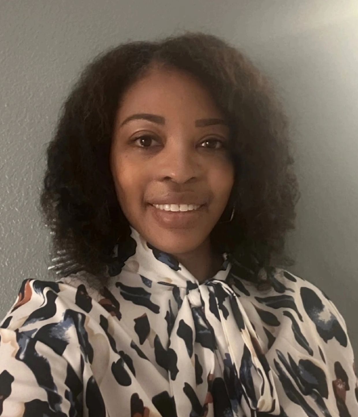 Smiling woman with curly hair and patterned blouse.