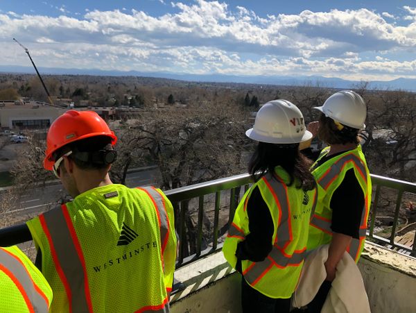 Three people on a balcony 40 feet in the air overlooking 88th Avenue and development to the south.
