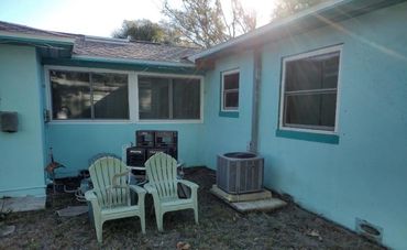 Two plastic chairs in a backyard corner with air conditioning unit.