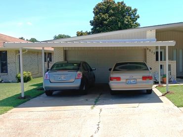 Attached red steel C-beam steel carport that the framing members has been painted installed in OKC