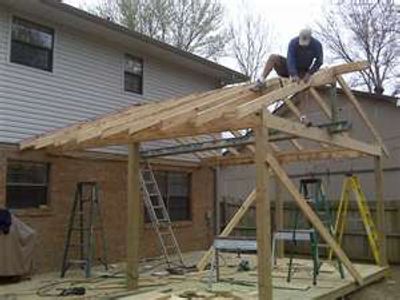Person building a wooden roof frame outdoors.