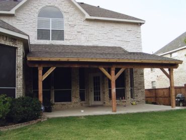 Backyard patio with wooden pergola attached to house.