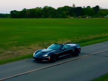 Aerial drone photo of dark blue 2018 corvette z06 driving on a road at sunset next to a farm field.