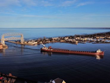 Aerial drone photo of Lake Superior cargo ship entering bay underneath the Duluth lift bridge.