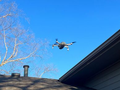 Photo of drone in the blue sky preforming a personal home inspection on a roof.
