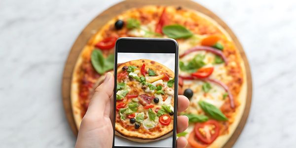 Person photographing a fresh vegetable pizza with a smartphone.