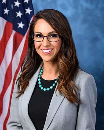 Professional woman with glasses and necklace in front of American flag.
