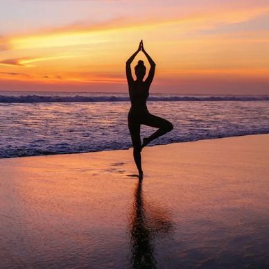Silhouette of a person practicing yoga on the beach at sunset.