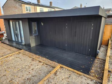 Modern black wooden garden office with deck and glass doors.