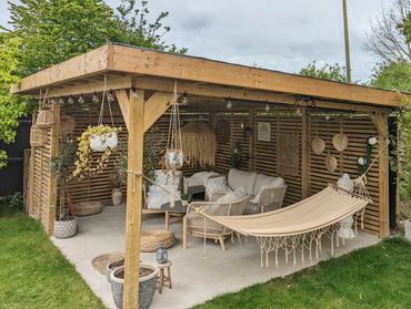 Cozy wooden gazebo with hammock and comfortable seating in a lush garden.