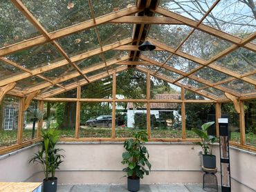 A spacious wooden-framed greenhouse with potted plants and outdoor view.
