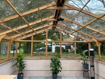 A spacious wooden-framed greenhouse with potted plants and outdoor view.